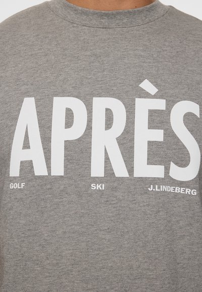 Szara koszulka z dużym białym napisem "APRÈS" oraz mniejszymi słowami "GOLF", "SKI" i "J.LINDEBERG" nadrukowanymi z przodu.