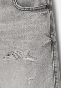 Jean en denim gris délavé présentant des zones usées avec des bords effilochés, une poche avant et des détails de couture subtils.