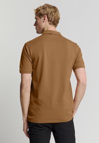 Bruine polo met korte mouwen en een kraag, gladde structuur, rechte snit, zichtbare stiksels en een eenvoudig ontwerp.