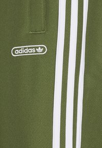 Grönt tyg med vitt Adidas-logotyp och tre vertikala vita ränder på högersidan.