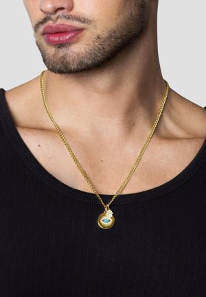 Guld halskæde med en cirkulær vedhæng med et øje-motiv og en turkis accent, båret over en sort ribbet skjorte.