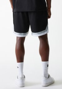 Black mesh athletic shorts with a white trim, featuring a loose fit and side pockets. Worn with white sneakers and matching socks.