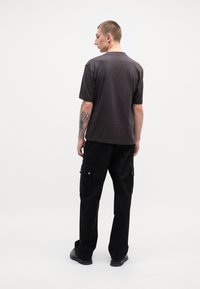 Dark gray short-sleeve t-shirt with a round neckline, paired with black cargo pants featuring pockets and snap button details, worn with black shoes.