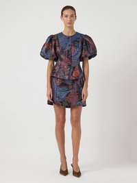 Γυναίκα που φοράει ένα εφαρμοστό πολύχρωμο φόρεμα με πούλιες, με φουσκωτά κοντά μανίκια και κοντή φούστα, συνδυασμένο με καφέ ψηλοτάκουνα παπούτσια slingback.