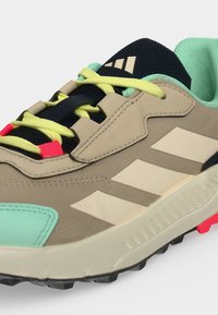 Μπεζ και μέντα αθλητικό παπούτσι Adidas με κίτρινα κορδόνια, κόκκινες λεπτομέρειες, μαύρη σόλα και τρεις άσπρες διαγώνιες ρίγες στην πλευρά.