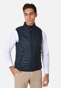 Gilet trapuntato Navy con alto colletto, chiusura frontale con zip e dettagli arancioni. Presenta due tasche laterali con zip ed è realizzato in materiale leggero.