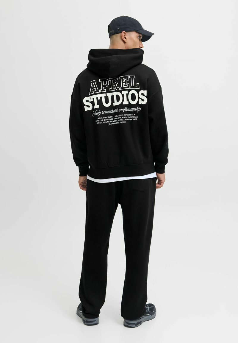 Schwarzer Hoodie mit dem Schriftzug "APREL STUDIOS" in Weiß auf dem Rücken, kombiniert mit schwarzen Sweatpants. Hat eine entspannte Passform und eine weiche Textur.