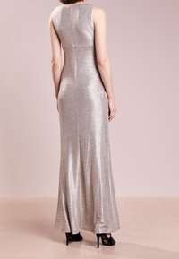Stříbrné, bezrukávové, dlouhé šaty s přiléhavým střihem a jemným leskem. Obsahují zadní zip a rozšířený lem.