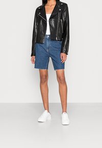 Svart lädermotorcykeljacka med silverdragkedjor, kombinerad med blå denimshorts med fransade kanter och vita sneakers.