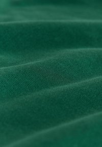 Gros plan sur un tissu vert montrant une texture fine en tricot et des plis doux.