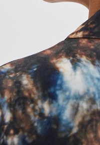 Kragenhemd mit einem mehrfarbigen abstrakten Muster, das dunkle Brauntöne, Blau- und Cremetöne enthält, aus glattem Stoff mit einer weichen Textur hergestellt.