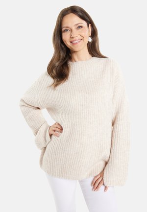 Cremfarbener, gerippter Strickpullover mit entspannter Passform, weiten Ärmeln und Rundhalsausschnitt, kombiniert mit weißen Hosen. Weicher Stoff und leichtes Gewicht.