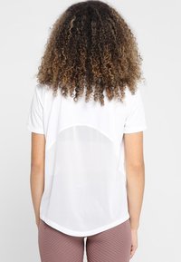 Camisa blanca de manga corta con panel trasero de malla, dobladillo redondeado y corte relajado. Combinada con leggings texturizados de color rosa claro.