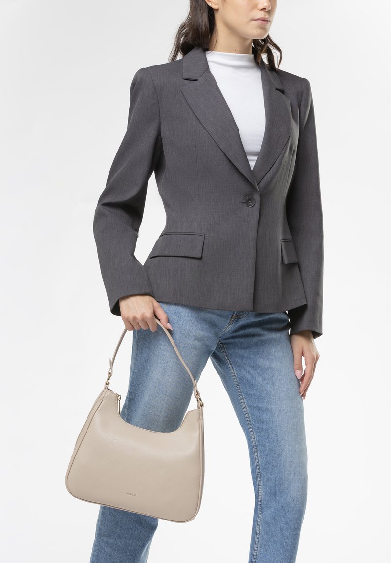 Blazer grigio su misura con un solo bottone e tasche laterali, abbinato a jeans azzurri chiari. Borsa in pelle color crema con forma curvata.