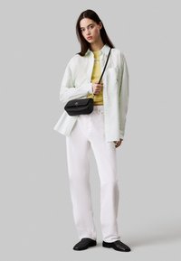 Pantaloni bianchi a gamba larga, camicia button-up verde chiaro, top aderente giallo e una borsa a tracolla nera. Texture morbide e design casual.