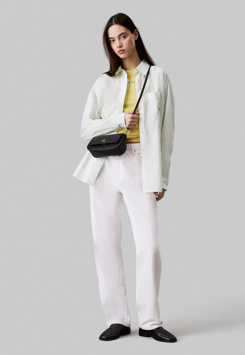 Pantaloni bianchi a gamba larga, camicia button-up verde chiaro, top aderente giallo e una borsa a tracolla nera. Texture morbide e design casual.