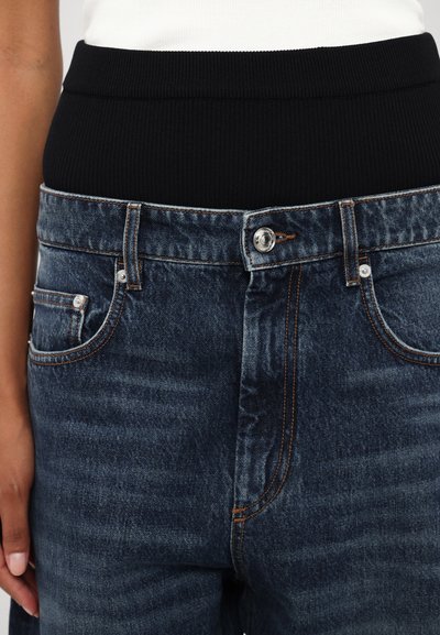 Jeans in denim blu scuro con una fascia in vita a coste nera. Dettagli di cucitura visibili e design classico a cinque tasche.