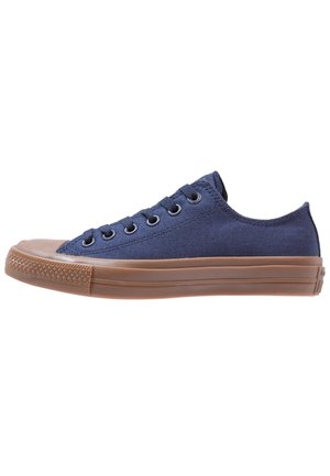 Chaussures basses en toile bleue avec une semelle en caoutchouc marron, bout rond, six œillets et accents texturés sur les côtés.