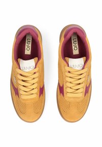 Paire de baskets en daim jaune avec des accents bordeaux, des lacets crème et des semelles intérieures de marque, vues de dessus sur un fond blanc.