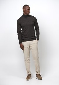 Dunkelgrauer Rollkragenpullover, beige Cordhosen und braune Sneakers, getragen von einer männlichen Person in einem neutralen Hintergrund.