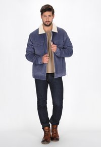 Granatowa kurtka z bawełnianego kordurowego materiału z kremowym, sztucznym kołnierzem z owczej wełny, dwoma kieszeniami na piersi i zapięciem na guziki. Nosisz ją na beżowej koszuli i dżinsach.