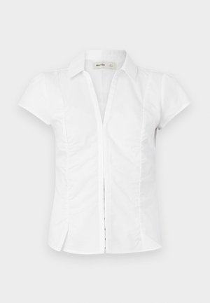 Blouse blanche à manches courtes avec un col à revers, des côtés plissés et des détails de coutures verticales. Fabriquée dans un tissu lisse et léger.