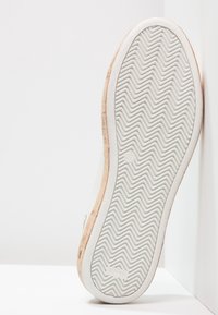 Vit gummisneakersula med ett texturerat zigzag-mönster, med en beige detalj längs kanten och minimal märkning på ytan.