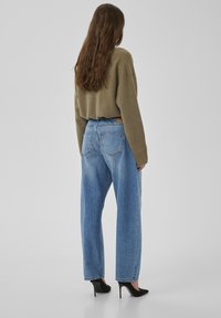 Pull olive vert raccourci et jean taille haute bleu clair. Tenue associée à des talons aiguilles noirs, vue de dos.