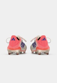 Valged ja roosad Adidas jalgpalliketsid siniste triipudega, vaadatuna tagant valgel taustal.