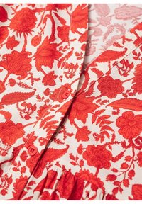 Tissu à motif floral rouge présentant diverses plantes et fleurs, avec un fond crème. Fermeture à deux boutons visible au niveau du col.