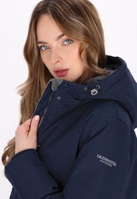 Navyblauwe hoodie met rits, grijze fleece voering en merkembleem op de mouw. Soepele textuur en verstelbare functies.