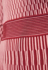 Tissu tricoté présentant un motif alterné de rayures verticales et de lignes en rouge et rose. Texture lisse avec un léger éclat.