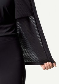 Schwarzes Sporttop mit strukturiertem, offenem Mesh-Ärmel, das einen figurbetonten Schnitt und eine gerade Passform aufweist. Glattes Material ohne sichtbare Hardware.