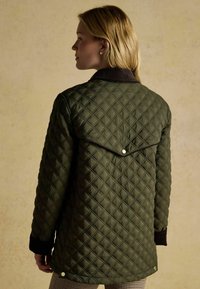 Zielona pikowana kurtka w diamentowy wzór, z ciemnym kołnierzem i detalami na zatrzaski. Posiada długie rękawy i teksturowany materiał.