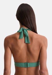 Mujer con cabello largo y oscuro que lleva un top de bikini verde tipo halter atado al cuello y sujetado por detrás, vista desde atrás.