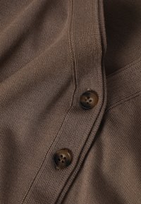 Tissu de cardigan tricoté brun avec deux boutons brun foncé attachés le long d'une couture côtelée.