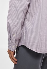 Lila randig långärmad skjorta med knäppte manschetter, med en etikett vid fållen, tillverkad av ett strukturerat tyg.