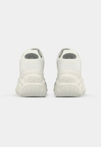 Vita sneakers med en slät läderöverdel, rundad design, stor dämpad häl och ribbad gummisula. Varumärke synligt på hälen.