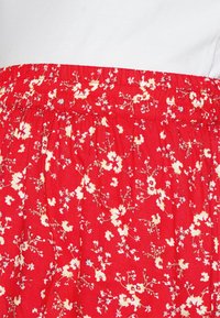 Vestido floral vermelho com cintura elástica franzida, apresentando padrões florais brancos e azul claro numa textura de tecido.