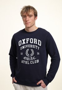 Navyblauw sweatshirt met een ronde halslijn en geribde manchetten, met witte opdruk "OXFORD UNIVERSITY ATHL CLUB" en een laurierontwerp.