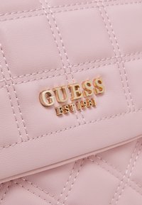 Różowa pikowana torebka z sztucznej skóry z złotym logo "GUESS" oraz napisem "EST 1981", z wyraźnymi akcentami przeszyć.
