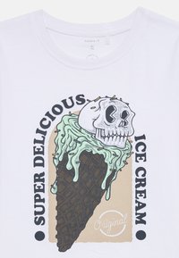 T-shirt en coton blanc avec un motif représentant un cornet de glace avec un crâne, une glace à la menthe et un motif de gaufre marron. Texte : "GLACE SUPER DÉLICIEUSE."