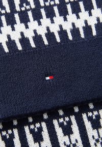Bonnet tricoté bleu marine avec un motif géométrique blanc, doté d'une bordure côtelée et d'un petit logo rouge, blanc et bleu sur le bord.