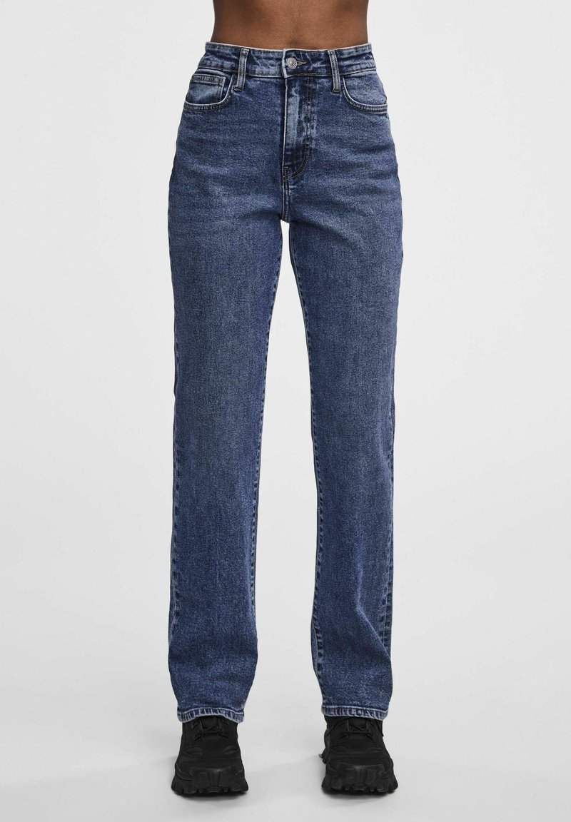 Dunkelblaue Jeans aus Denim mit hoher Taille, geradem Beinschnitt, Fünf-Taschen-Design und dezenter Used-Optik, kombiniert mit schwarzen Schuhen.