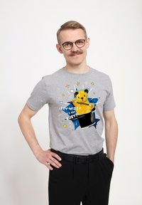 Šedé tričko s krátkým rukávem s barevným grafickým motivem medvěda a textem "IZZY WIZZY, POJĎME SE ZAPOJIT!" s akcenty ve tvaru hvězdného výbuchu.
