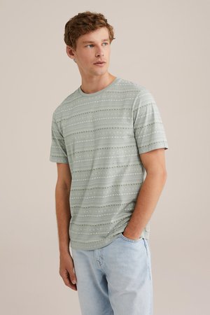 T-shirt en coton à manches courtes de couleur vert clair, avec des rayures horizontales et des motifs variés dans des teintes plus foncées, encolure ras du cou. Coupe décontractée.
