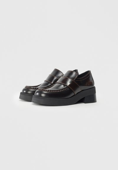 Brown leather loafers with raised stitching, two horizontal leather straps, and a thick black rubber sole. Smooth texture with glossy finish.