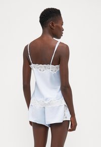 Vaaleansininen satiininen topin ja shortsien setti, jossa on herkkä valkoinen pitsireunus hemman ja hihnojen ympärillä, sileä rakenne ja rento istuvuus.