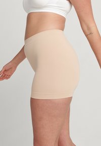 Beige naadloze shapewear shorts met een hoge tailleband, een gladde textuur en een aansluitend ontwerp, geschikt voor het dragen onder kleding.