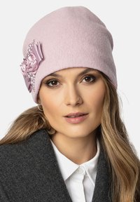 Căciulă roz din lână, cu un vârf rotund, având un accent floral roz și detalii cu perle pe o parte. Materialul are un aspect moale și texturat.